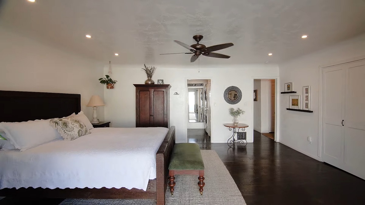A spacious bedroom with elegant furniture, dark wood flooring, and a ceiling fan creating a serene atmosphere