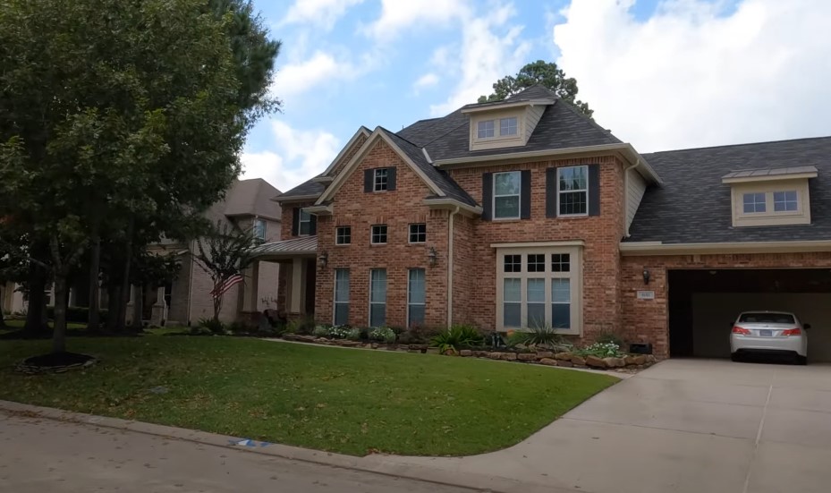 A large, two-story brick home with a dark gray roof sits on a well-maintained lawn
