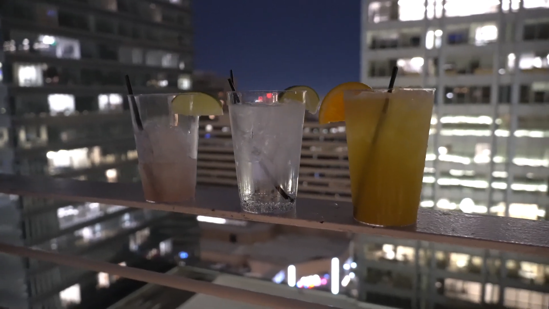 Three cocktails on a rooftop bar with city lights in the background