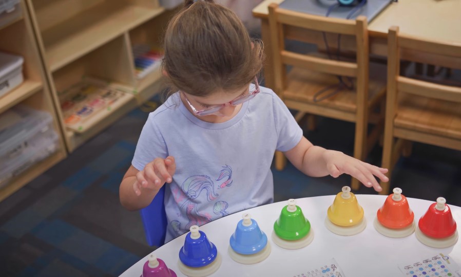 A young girl, focused and engaged, plays colorful handbells