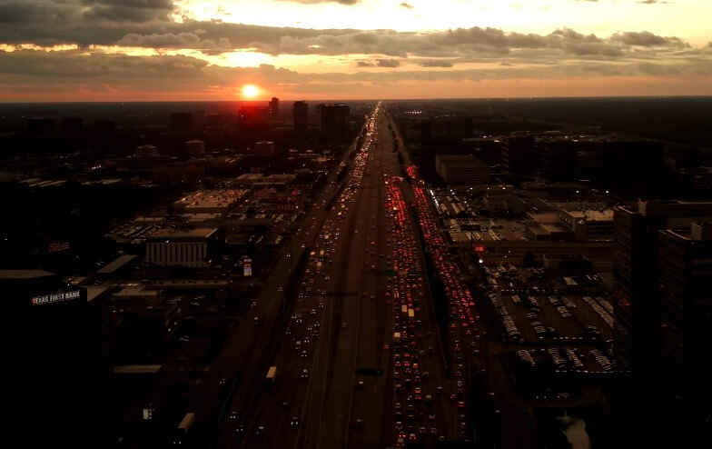 A sprawling highway, choked with traffic, stretches beneath a fiery sunset