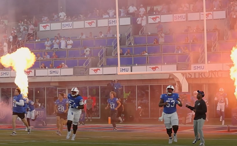 Football players in blue uniforms sprint across the field