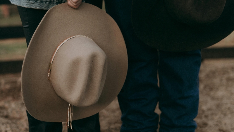 Two people hold cowboy hats by their sides