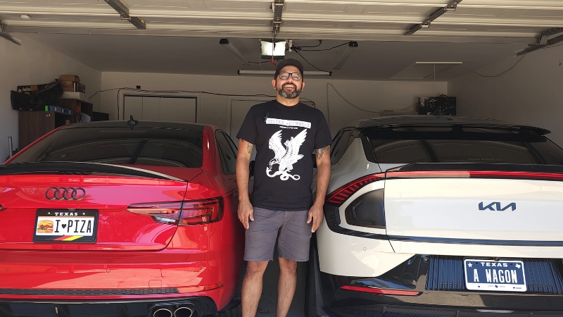 A man stands between two cars with Texas license plates inside a garage, showing personal Texas pride
