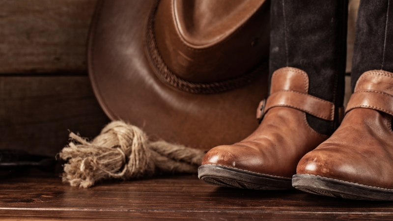 Brown cowboy boots, a hat, and a rope on a wooden floor