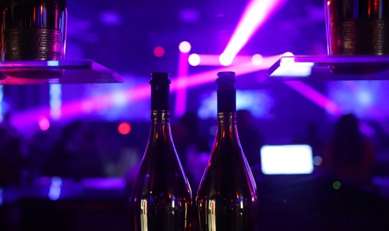 Two wine bottles sit on a bar illuminated by purple lights