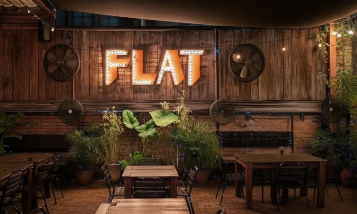 A restaurant patio with tables and chairs in front of a sign reading "Flat"