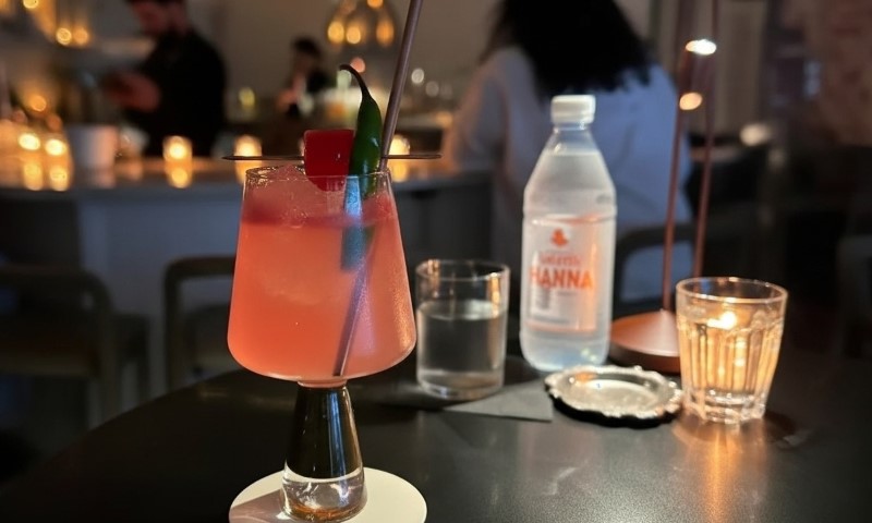 A pink drink on a table in front of a person, suggesting a casual setting or social gathering