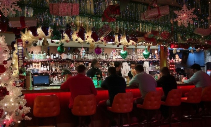 People sitting at a bar adorned with festive Christmas decorations, enjoying drinks and conversation