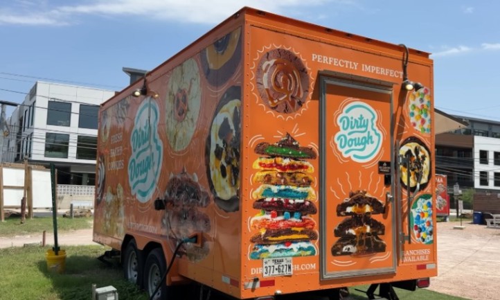 A food truck with a large orange trailer parked on the side of the road