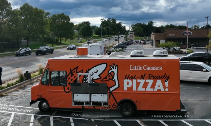 A pizza truck parked in a parking lot, ready to serve customers with delicious pizza options