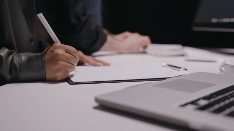 A person writes notes beside a laptop during a planning session