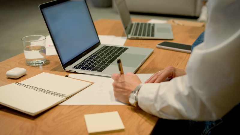 Person writes notes beside a laptop and notebook during business planning work