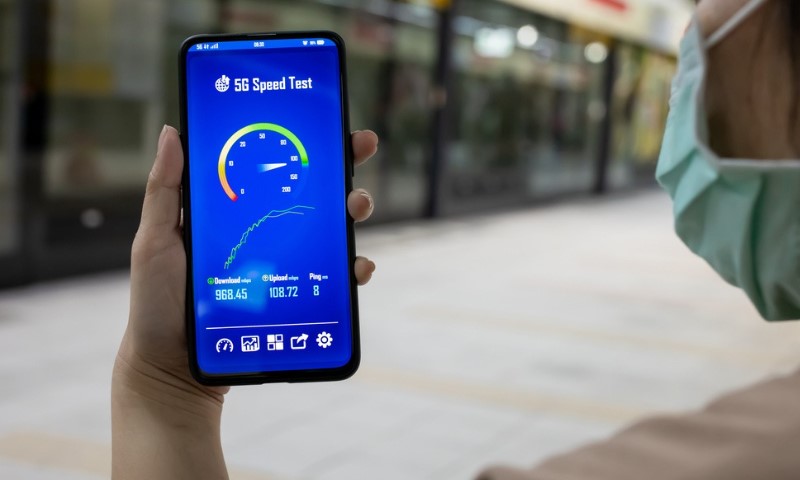 A person holding a smartphone displaying a 5G speed test app with results