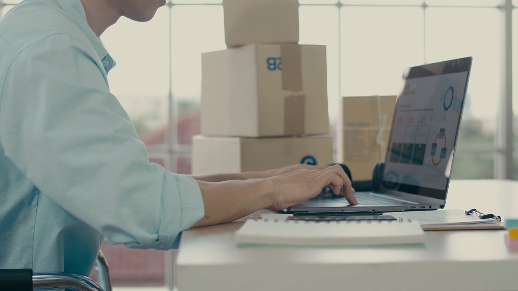 eCommerce operator working on a laptop with shipping boxes and order management tools nearby